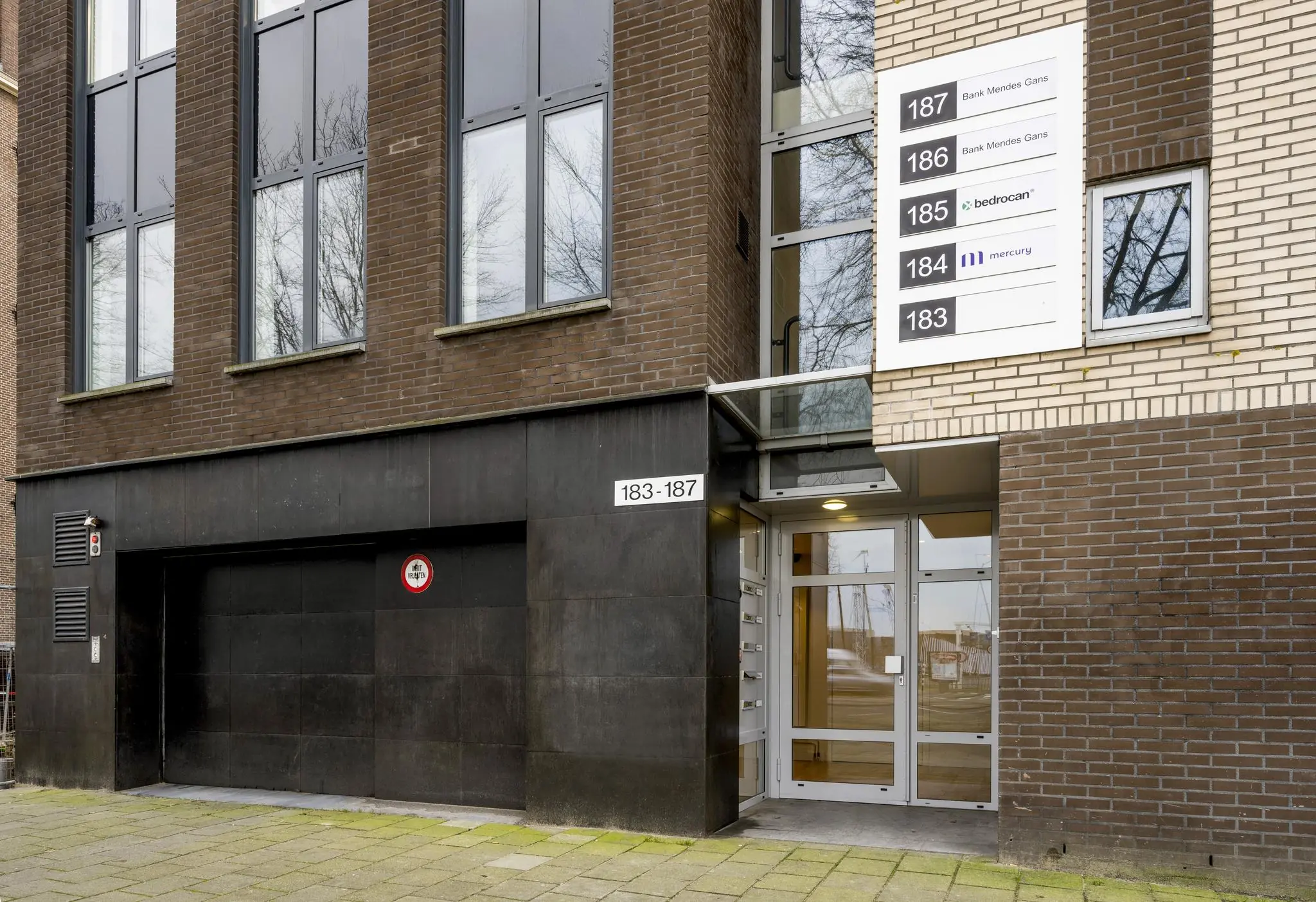 Ingang van een kantoorgebouw aan de Prins Hendrikkade met huisnummers 183-187 en bedrijfsnaambord naast de deur.